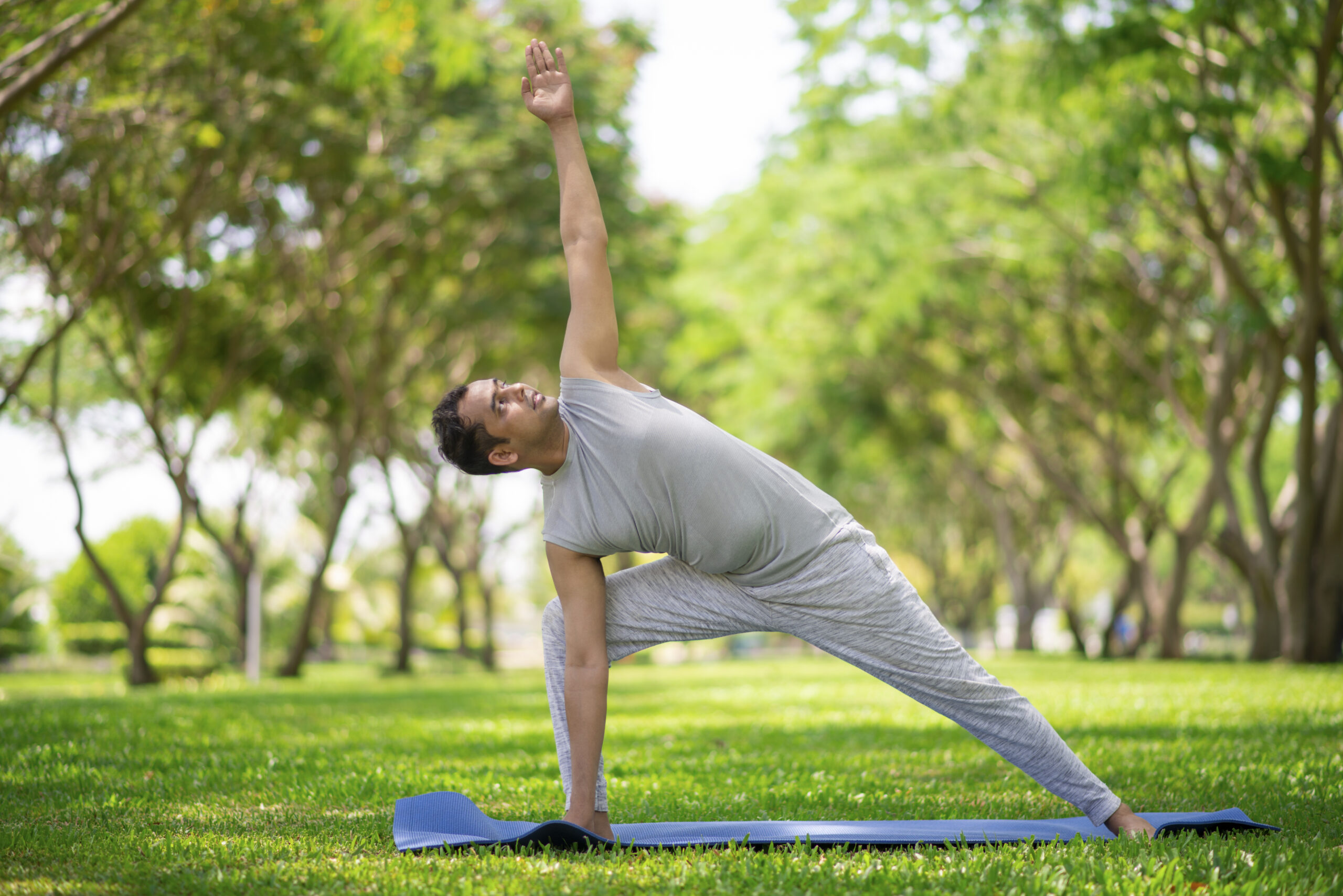 Inspired Indian man doing yoga asanas in city park. Young citizen exercising outside and standing in yoga side angle pose. Fitness outdoors and life balance concept